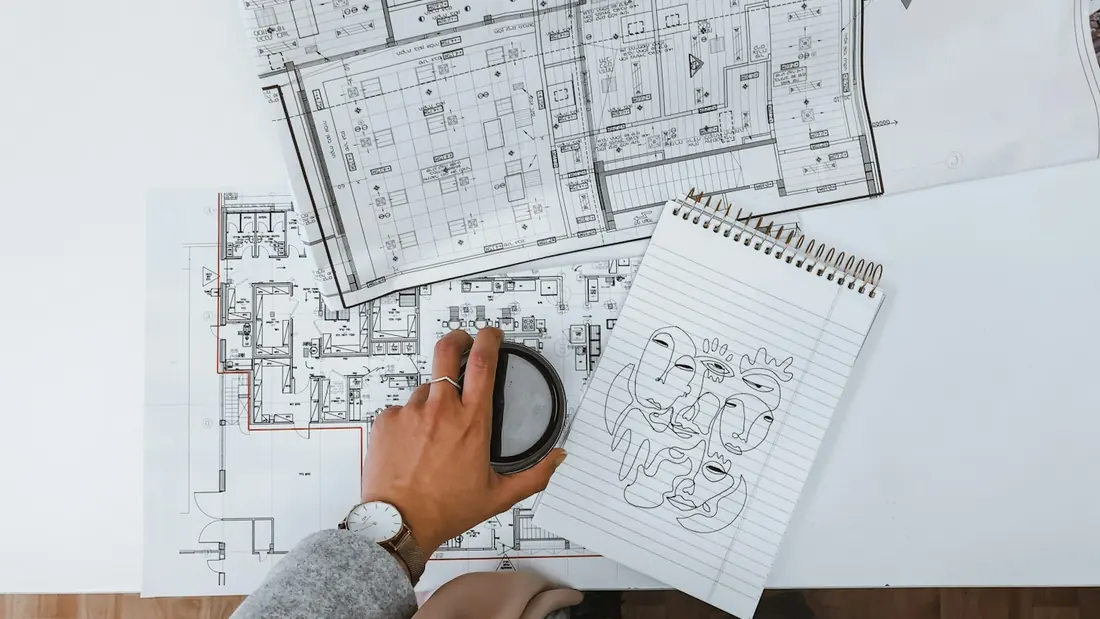 Floor plan drawings on a desk beside a keyboard and mouse